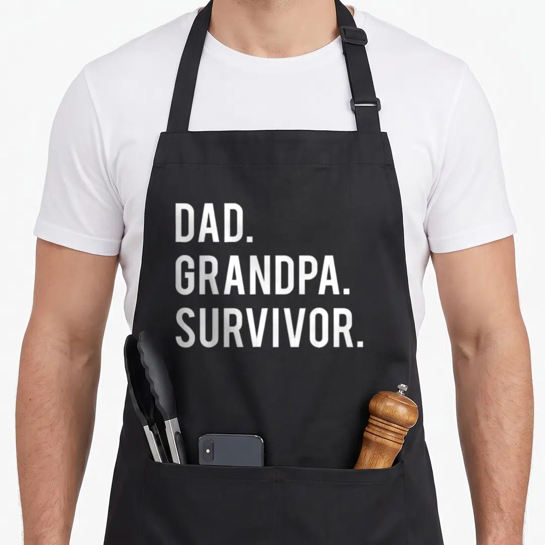 Survivor grandpa apron - White text DAD GRANDPA SURVIVOR stacked on black apron — shown on a black cotton canvas apron against a white background