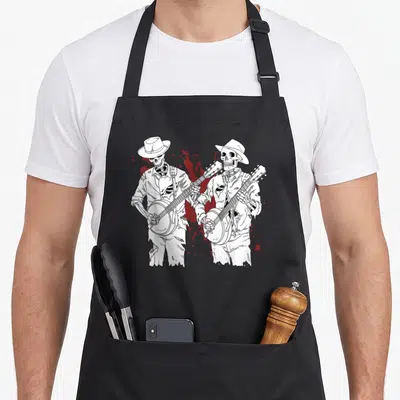 Scary skeleton apron - Two white line-art skeletons in hats playing banjos with red splatters — shown on a black cotton canvas apron against a white background