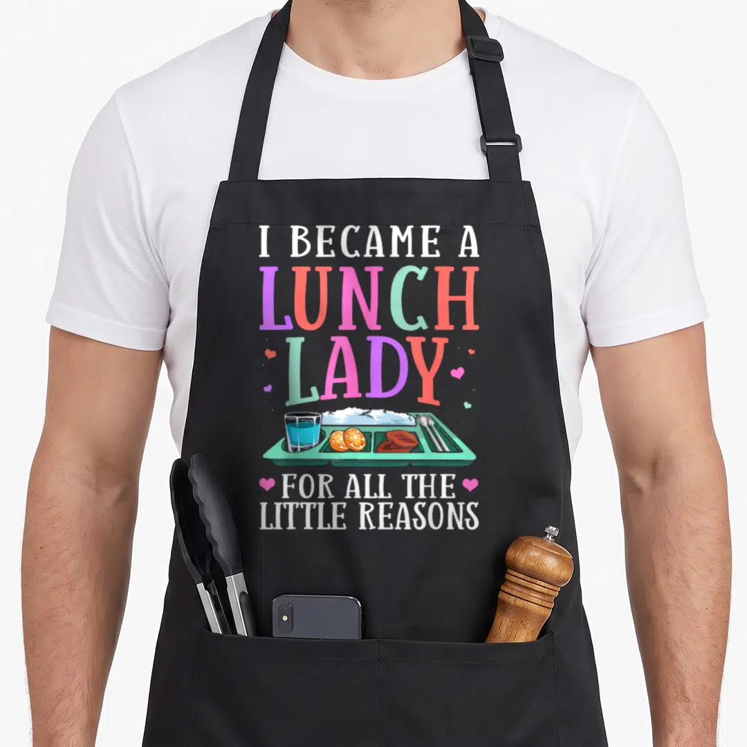 Reason lunch lady apron - Cartoon lunch tray with rice, meat, fruit and colorful text reading I became a lunch lady — shown on a black cotton canvas apron against a white background