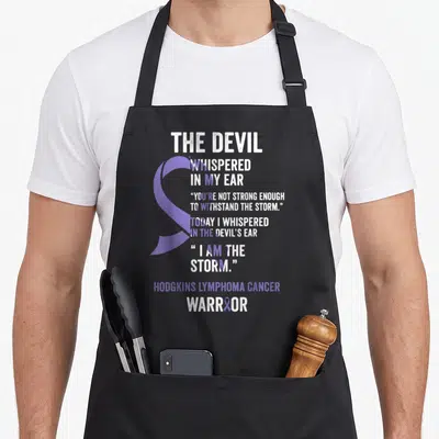 Hodgkin devil's apron - Purple ribbon behind white distressed text reading I AM THE STORM and Hodgkins Lymphoma Cancer — shown on a black cotton canvas apron against a white background