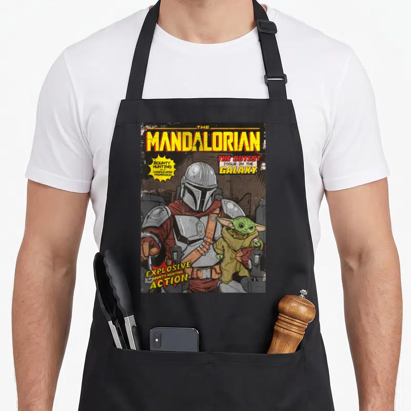 Vintage comic cover apron - Mandalorian comic cover print with yellow and silver text bubbles on black background — shown on a black cotton canvas apron against a white background