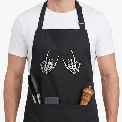 Rocker hand skeleton apron - Two white skeletal hands making the rock gesture in line art on black — shown on a black cotton canvas apron against a white background