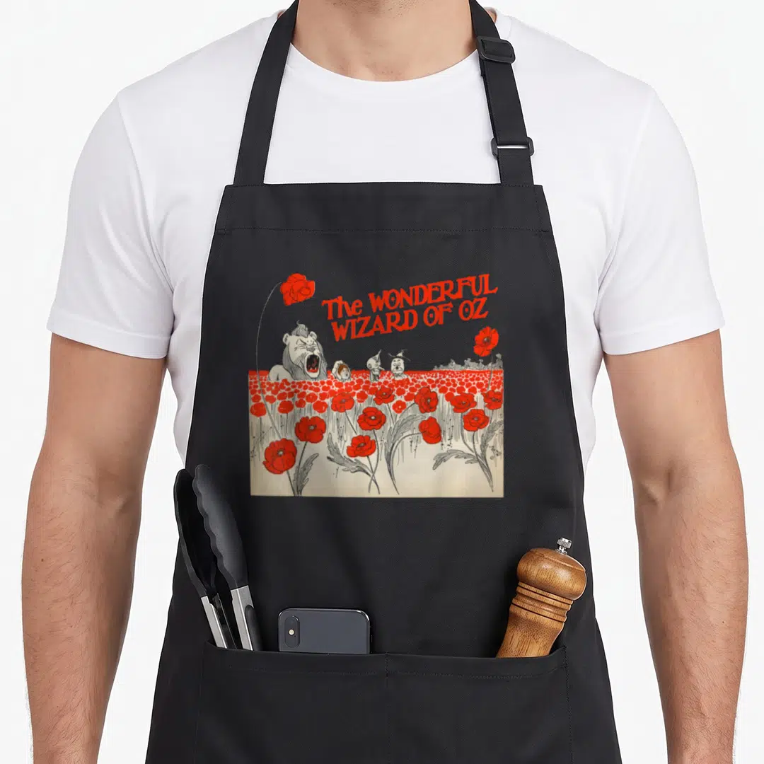 Wizard tin dorothy apron - Red poppy field with four characters and arched title text in cartoon style — shown on a black cotton canvas apron against a white background