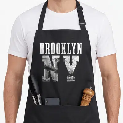 Retro brooklyn new york apron - Distressed white BROOKLYN text above grey NY letters containing a bridge and skyline — shown on a black cotton canvas apron against a white background