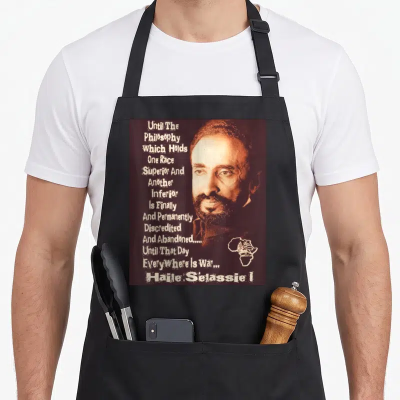 Emperor lion apron - Haile Selassie I portrait with anti-racism quote and Africa map outline in brown and white — shown on a black cotton canvas apron against a white background