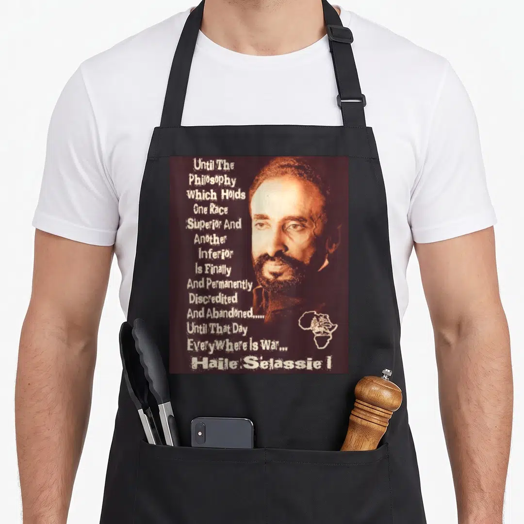Emperor lion apron - Haile Selassie I portrait with anti-racism quote and Africa map outline in brown and white — shown on a black cotton canvas apron against a white background