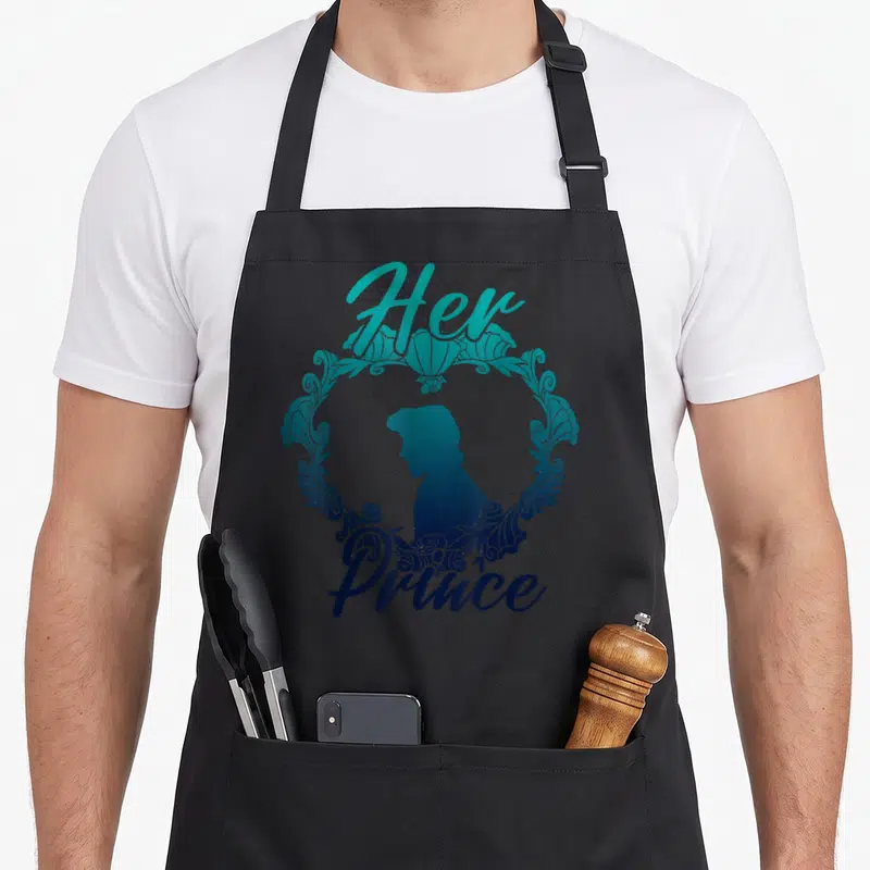 Eric couple apron - Her Prince text framing a teal blue gradient man silhouette in ornate circle — shown on a black cotton canvas apron against a white background