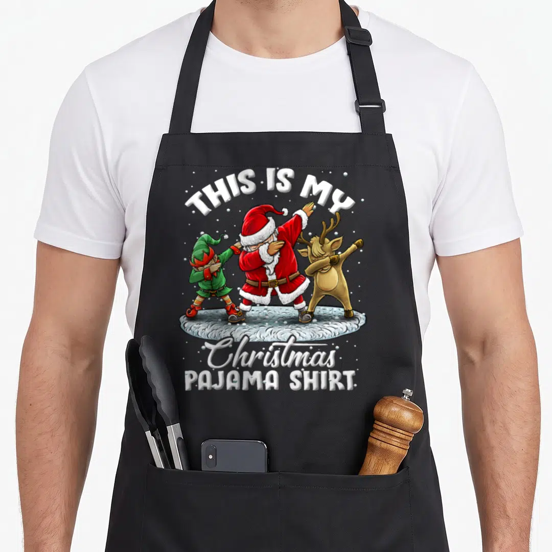 Pajama christmas elf apron - Dabbing Santa elf and reindeer with THIS IS MY Christmas PAJAMA SHIRT text — shown on a black cotton canvas apron against a white background