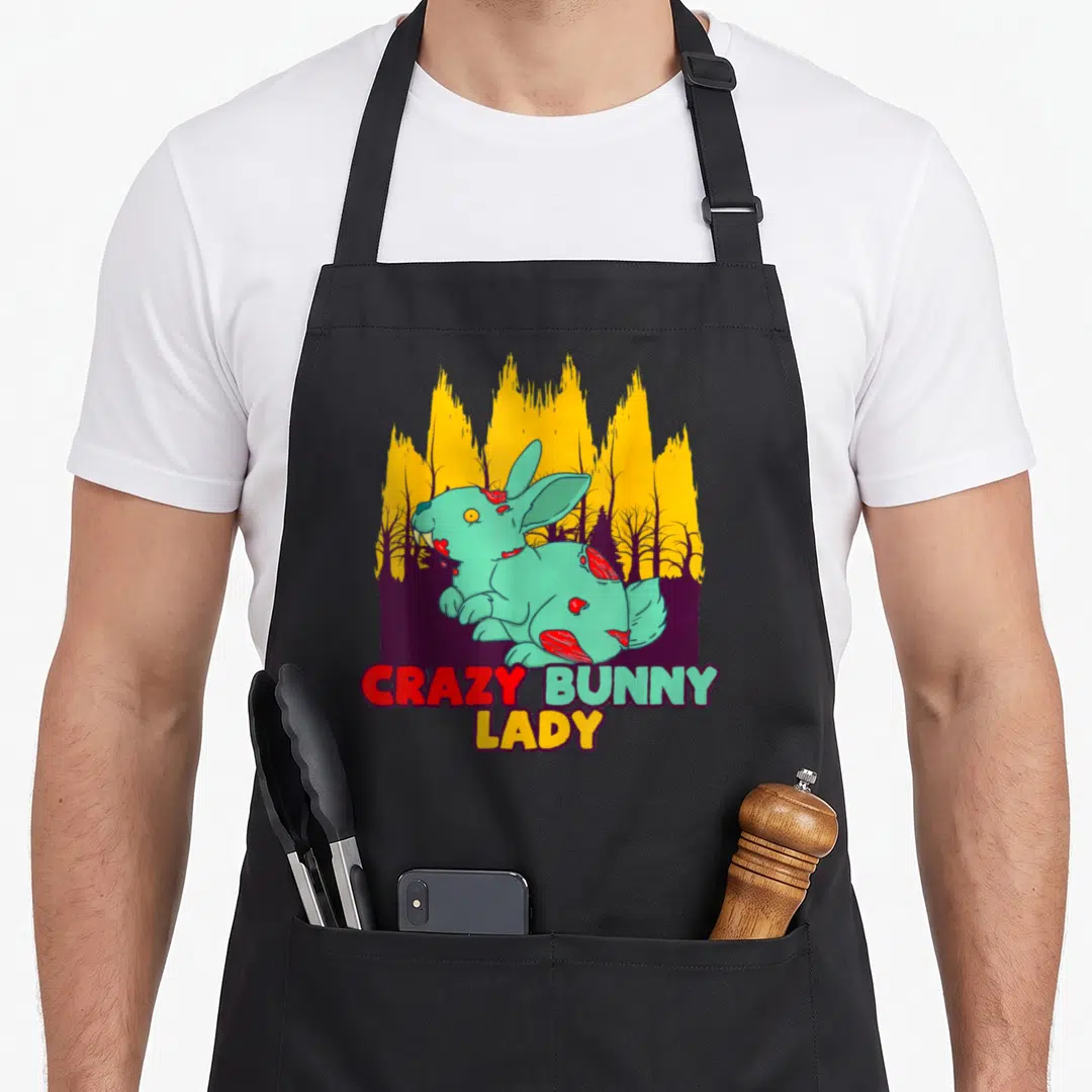 Bunny zombie halloween apron - Teal zombie rabbit with red wounds and CRAZY BUNNY LADY text over yellow trees — shown on a black cotton canvas apron against a white background
