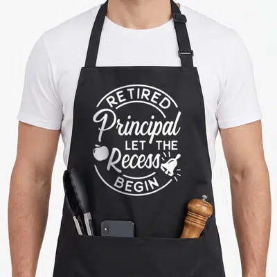 Principal retirement apron - White circular text design with apple and bell symbol reading Retired Principal — shown on a black cotton canvas apron against a white background