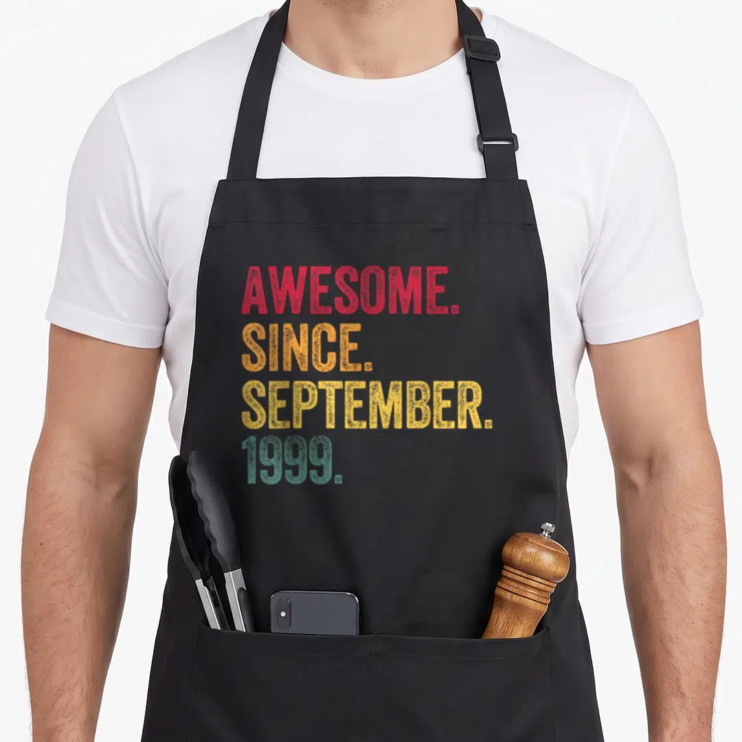 September 26th birthday apron - Stacked distressed text reading AWESOME SINCE SEPTEMBER 1999 in red orange yellow — shown on a black cotton canvas apron against a white background