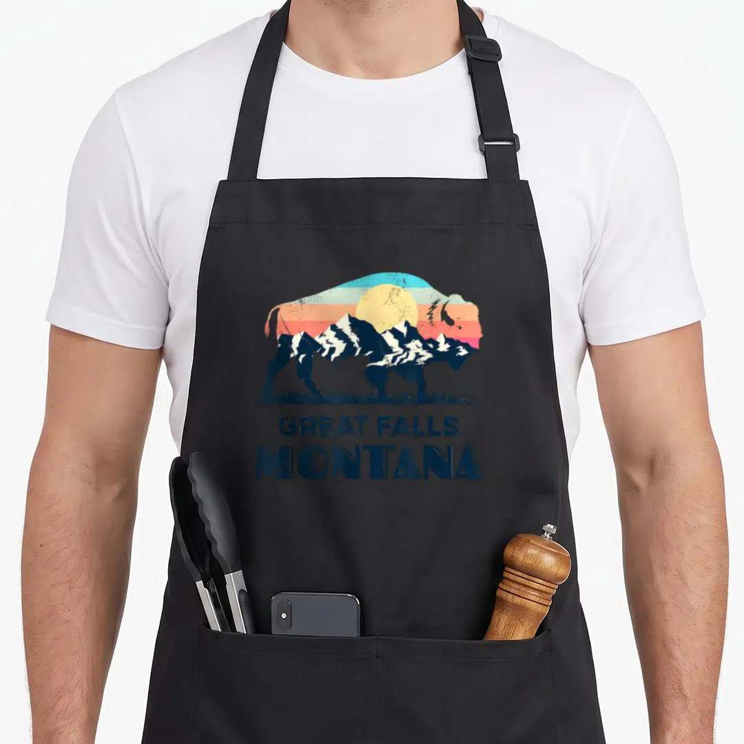 Hiking cute fall aprons - Retro bison silhouette with striped sunset and Great Falls Montana text — shown on a black cotton canvas apron against a white background