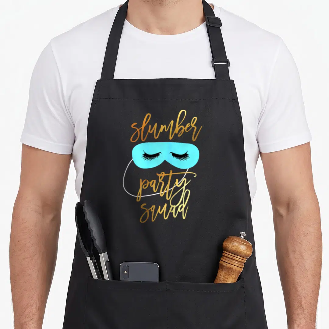 Slumber teyliedesign apron - Light blue sleep mask with black lashes and gold slumber party squad script — shown on a black cotton canvas apron against a white background