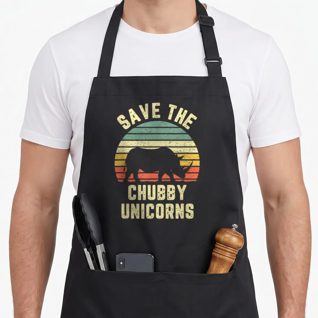 Chubby rhino unicorn apron - Retro rhino silhouette inside striped sun with text Save The Chubby Unicorns — shown on a black cotton canvas apron against a white background