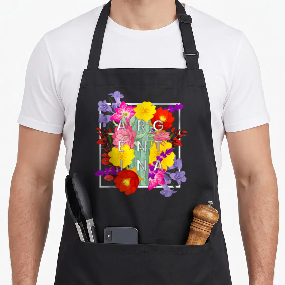 Flower argentine pride apron - Vertical ARGENTINA text over realistic pink yellow red purple flowers and cactus — shown on a black cotton canvas apron against a white background