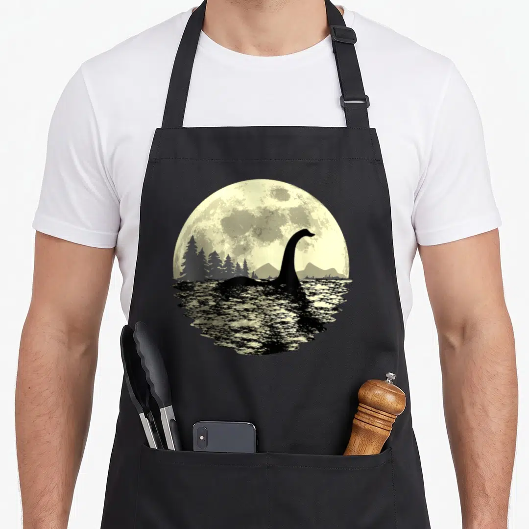 Moonlight loch ness monster apron - Black plesiosaur silhouette rising from water against a large pale yellow moon — shown on a black cotton canvas apron against a white background