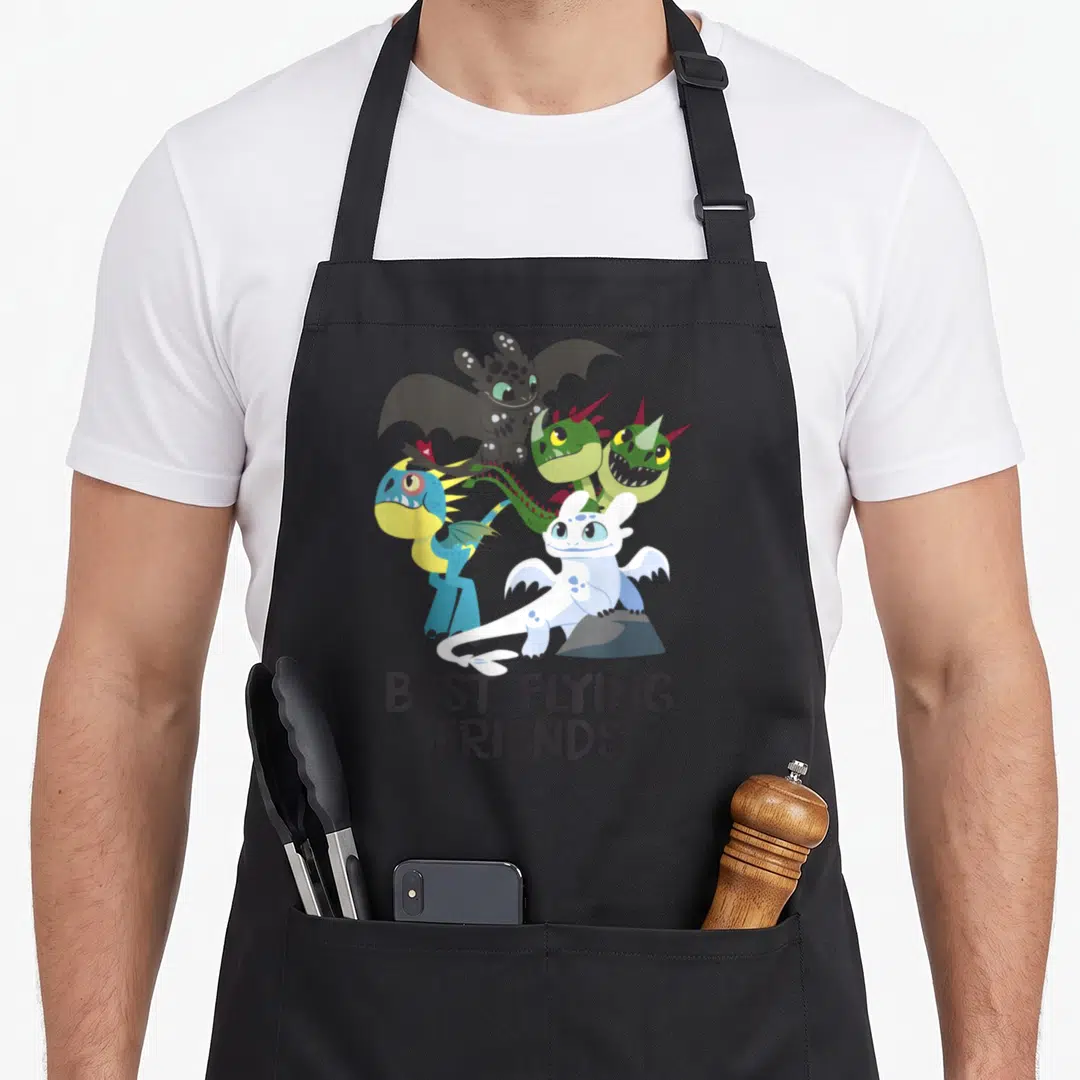 Train friends apron - Five cartoon dragons above BEST FLYING FRIENDS text in black white green blue yellow — shown on a black cotton canvas apron against a white background