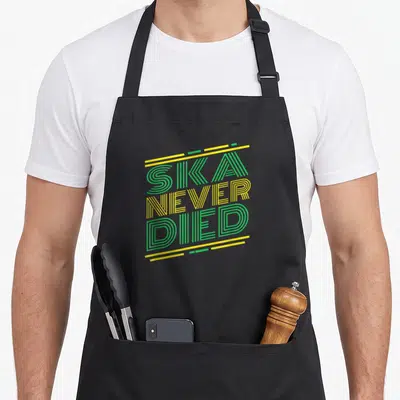 Jazz ska apron - SKA NEVER DIED text in green and yellow stacked typography with horizontal lines — shown on a black cotton canvas apron against a white background