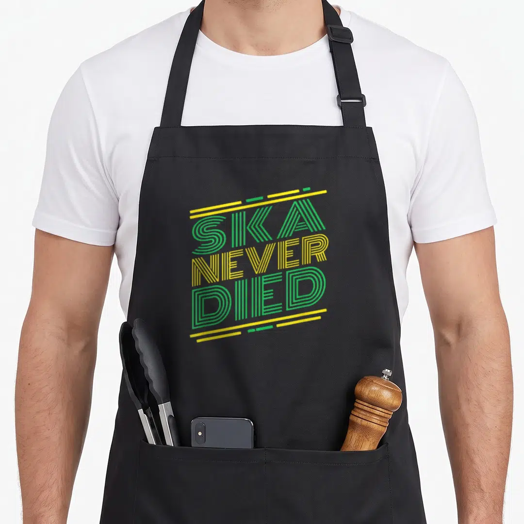 Jazz ska apron - SKA NEVER DIED text in green and yellow stacked typography with horizontal lines — shown on a black cotton canvas apron against a white background