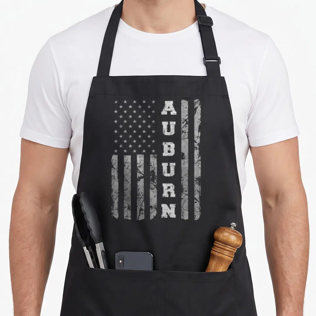 Flag alabama apron - Distressed white USA flag with vertical AUBURN text replacing a stripe — shown on a black cotton canvas apron against a white background