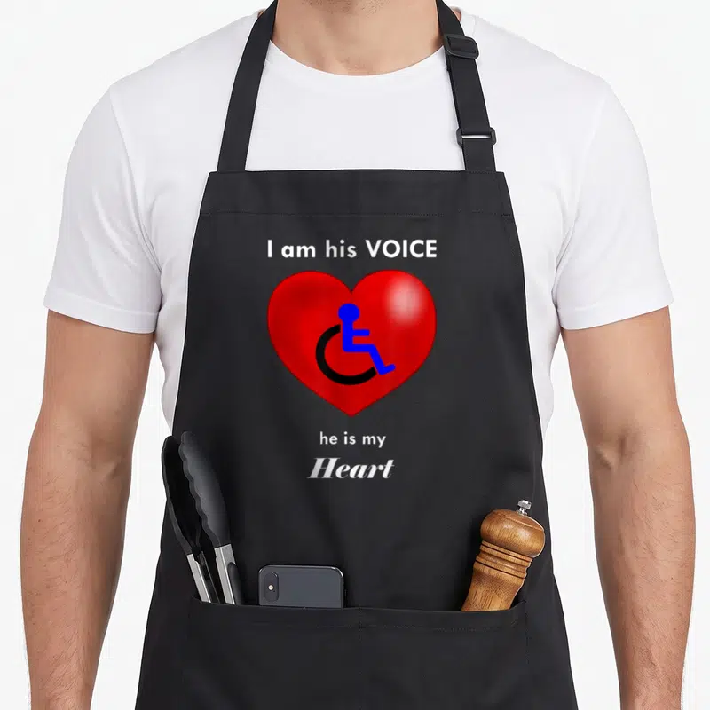 Funny wheelchair special aprons - Red heart with blue black wheelchair icon and white text I am his VOICE he is my Heart — shown on a black cotton canvas apron against a white background
