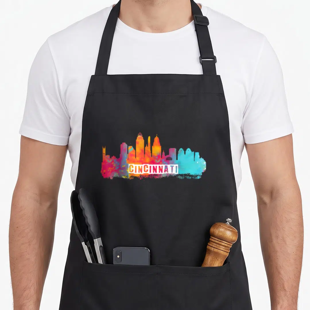 Watercolor pride apron - Multicolored watercolor Cincinnati skyline with white banner text across lower center — shown on a black cotton canvas apron against a white background