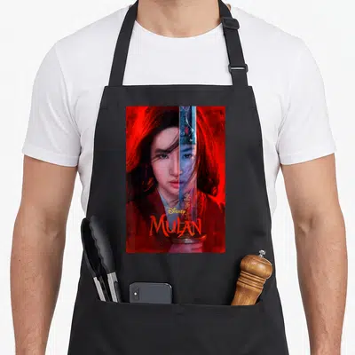Live split apron - Woman holding vertical sword, red background, Disney MULAN text — shown on a black cotton canvas apron against a white background