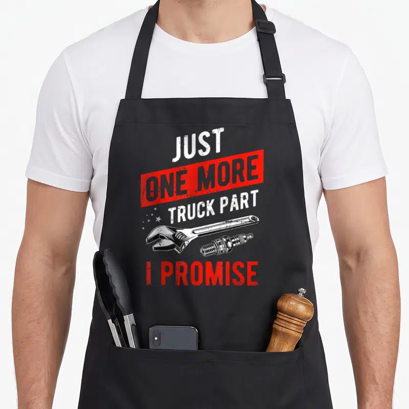 Part truck apron - Wrench and spark plug below red banner reading Just One More Truck Part I Promise — shown on a black cotton canvas apron against a white background