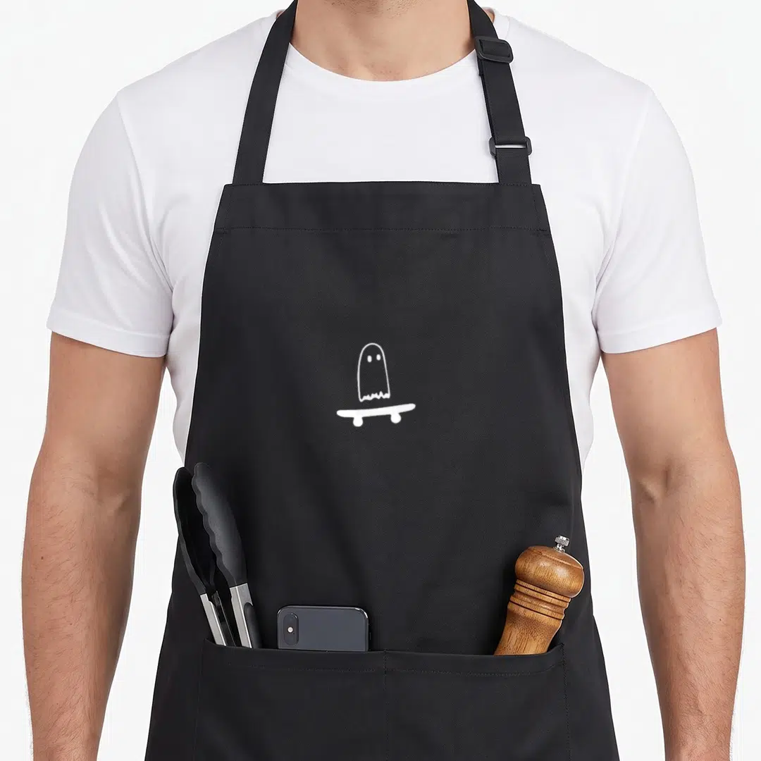 Ghost funny halloween aprons - White line art ghost standing on skateboard with two oval eyes — shown on a black cotton canvas apron against a white background