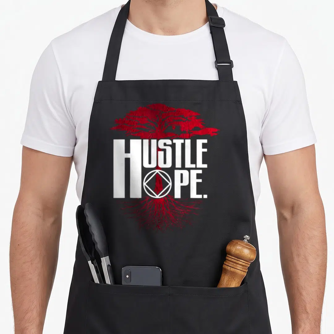 Anonymous narcotics recovery apron - Red tree graphic with HUSTLE HOPE text and sobriety circle diamond logo — shown on a black cotton canvas apron against a white background