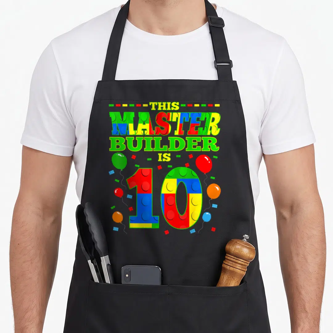 Log birthday apron - Number 10 made of red blue yellow and green bricks with balloons and text — shown on a black cotton canvas apron against a white background