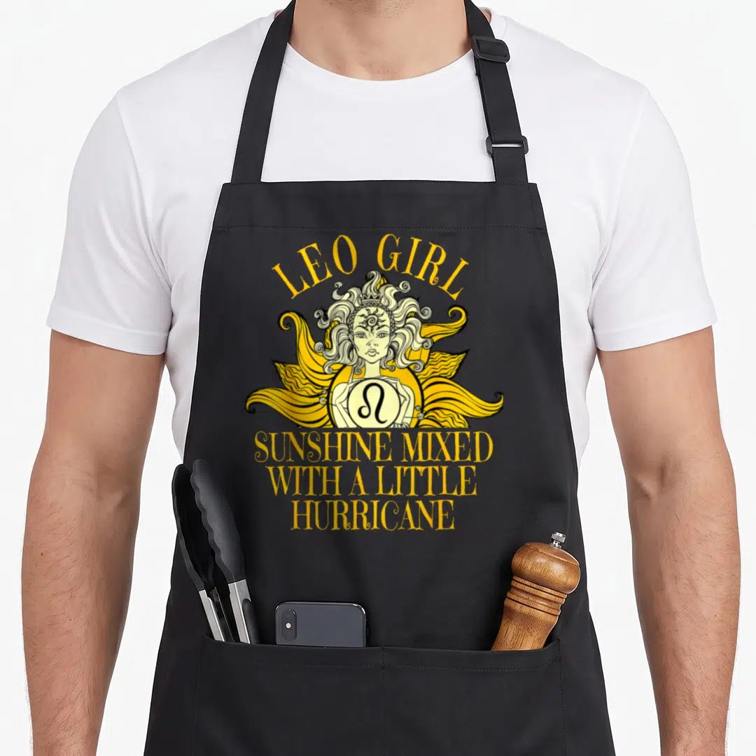 Sign july birthday apron - LEO GIRL text above yellow line-art girl holding Leo symbol with stacked hurricane quote — shown on a black cotton canvas apron against a white background