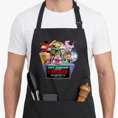 Jeff rochester apron - Caricature dummies in grey bin with Jeff Dunham Still Not Canceled text — shown on a black cotton canvas apron against a white background