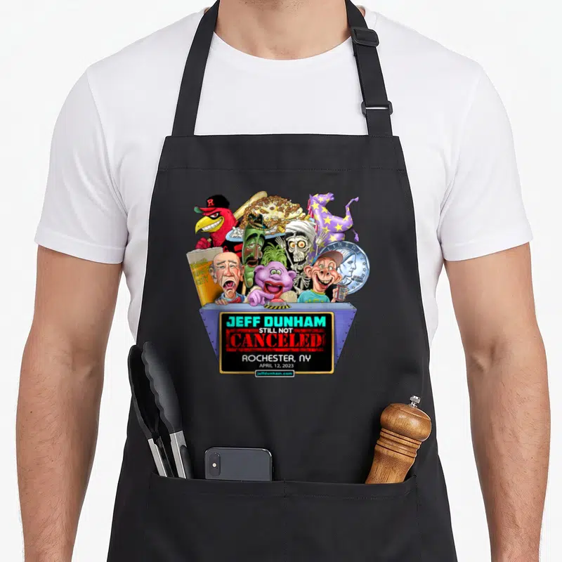 Jeff rochester apron - Caricature dummies in grey bin with Jeff Dunham Still Not Canceled text — shown on a black cotton canvas apron against a white background
