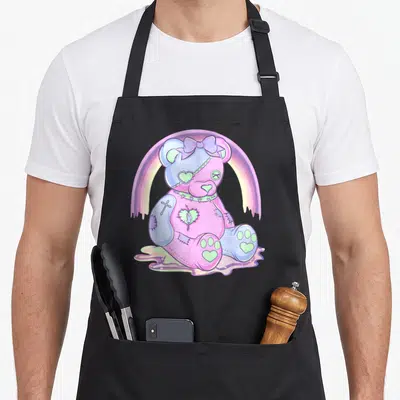 Pastel anime cooking apron - Patched teddy bear in pink purple blue and green sitting in liquid under dripping rainbow — shown on a black cotton canvas apron against a white background