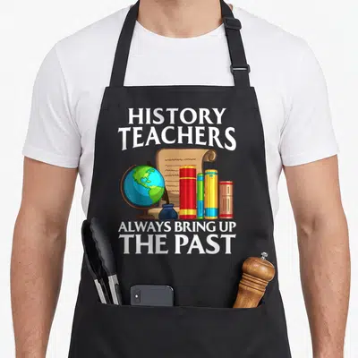 Social teacher apron - HISTORY TEACHERS text above globe scroll inkwell and books with ALWAYS BRING UP THE PAST below — shown on a black cotton canvas apron against a white background