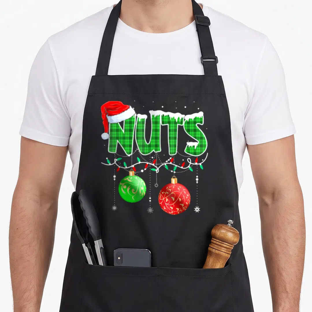 Nut family christmas aprons - NUTS text in green plaid with Santa hat, snow, lights, and two hanging ornaments — shown on a black cotton canvas apron against a white background