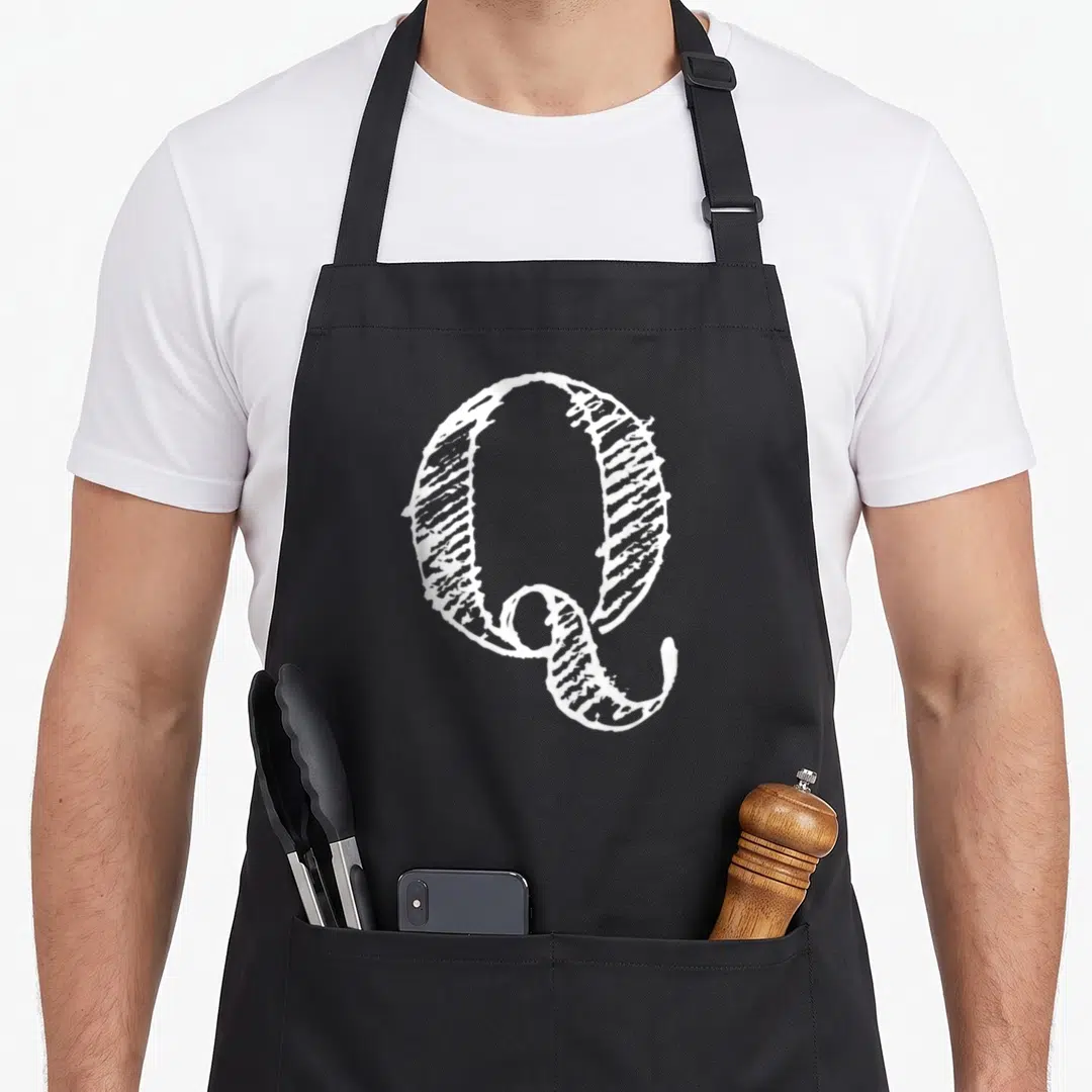 Bold decorative aprons - White textured capital letter Q printed on grey background — shown on a black cotton canvas apron against a white background