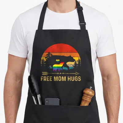Free cute bear apron - Rainbow bears and free mom hugs text on black apron — shown on a black cotton canvas apron against a white background