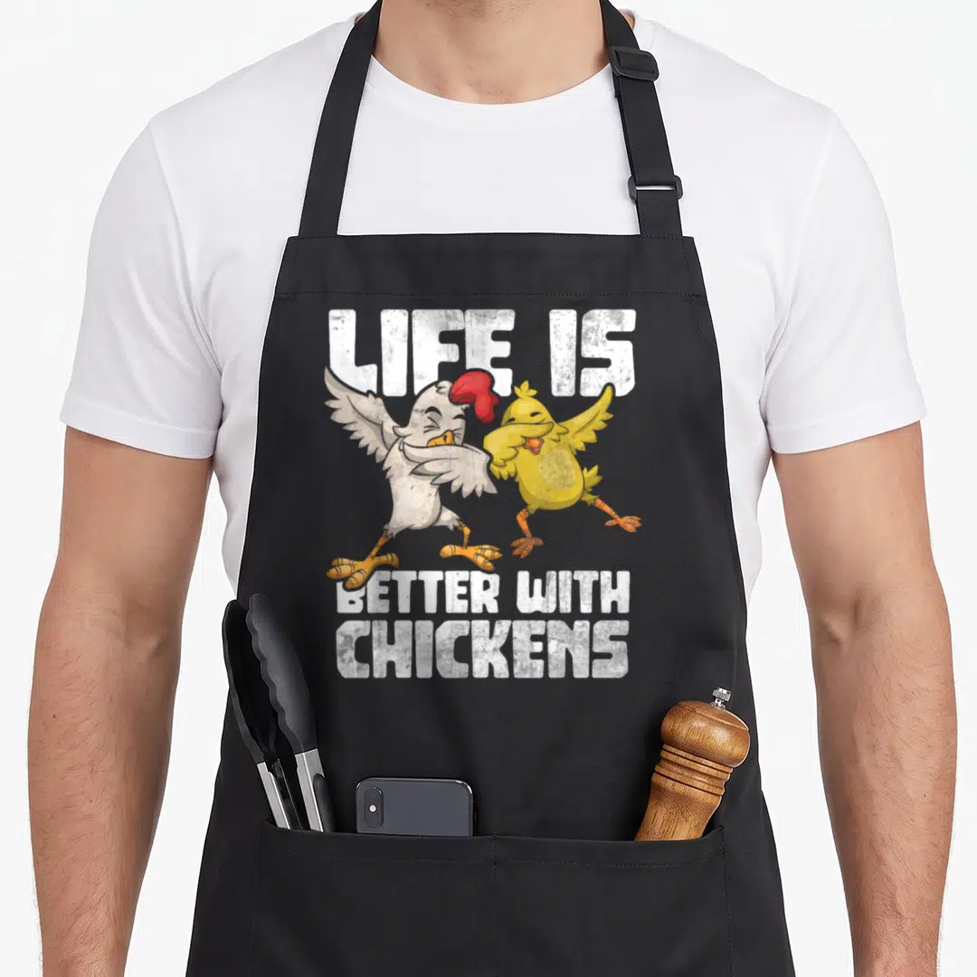 Animal hen apron - Two cartoon chickens dabbing between white text reading life is better with chickens — shown on a black cotton canvas apron against a white background