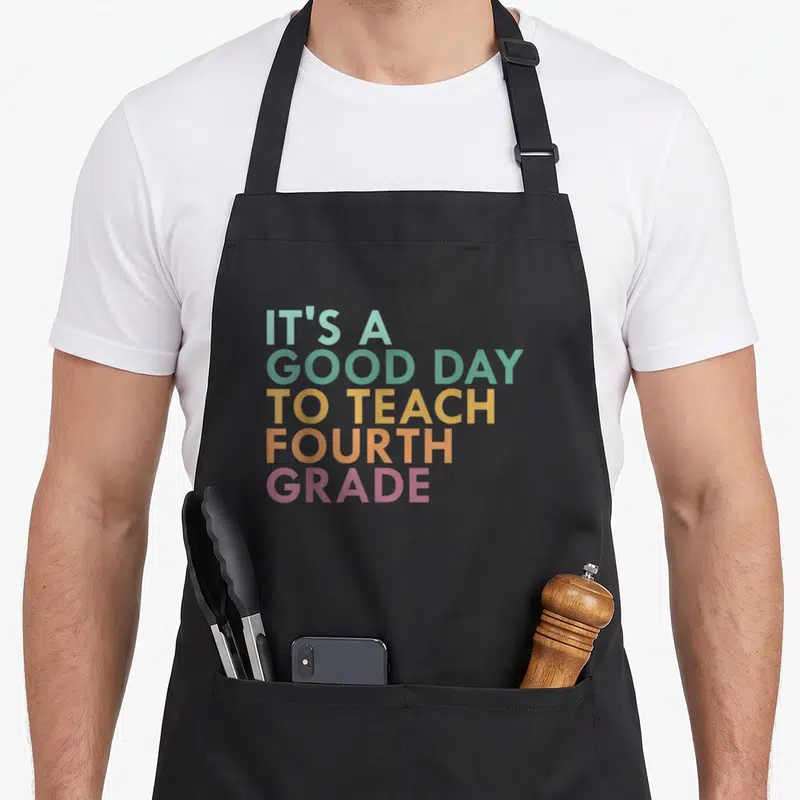 Teach fourth grade teacher apron - Stacked text reading IT'S A GOOD DAY TO TEACH FOURTH GRADE in pastel rainbow colors — shown on a black cotton canvas apron against a white background