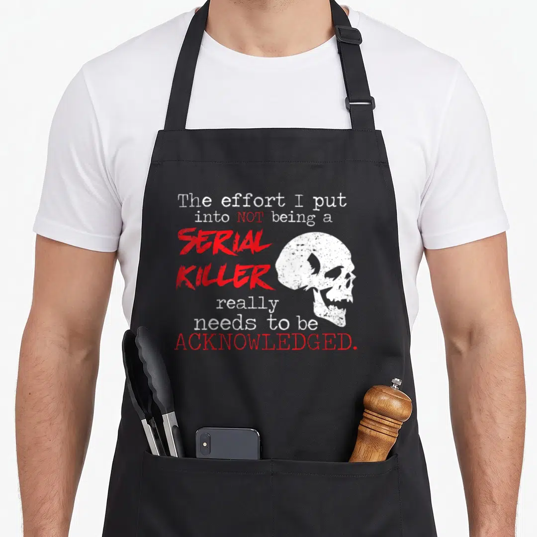 Serial novelty apron - Red and white text reading Serial Killer next to a white skull graphic — shown on a black cotton canvas apron against a white background