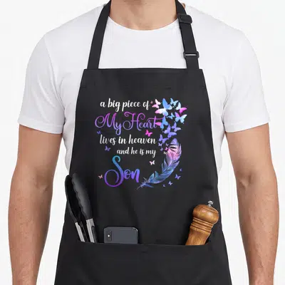 Live dad and son aprons - Watercolor butterflies and feather surrounding text about a son in heaven — shown on a black cotton canvas apron against a white background