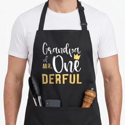 Onederful grandpa apron - Stacked white and yellow text Grandpa of MR One DERFUL with small gold crown accent — shown on a black cotton canvas apron against a white background