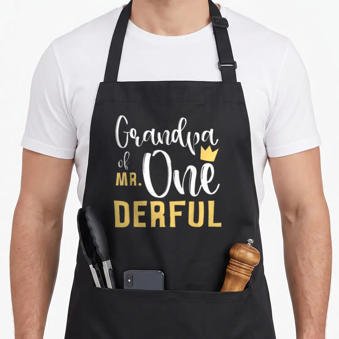 Onederful grandpa apron - Stacked white and yellow text Grandpa of MR One DERFUL with small gold crown accent — shown on a black cotton canvas apron against a white background
