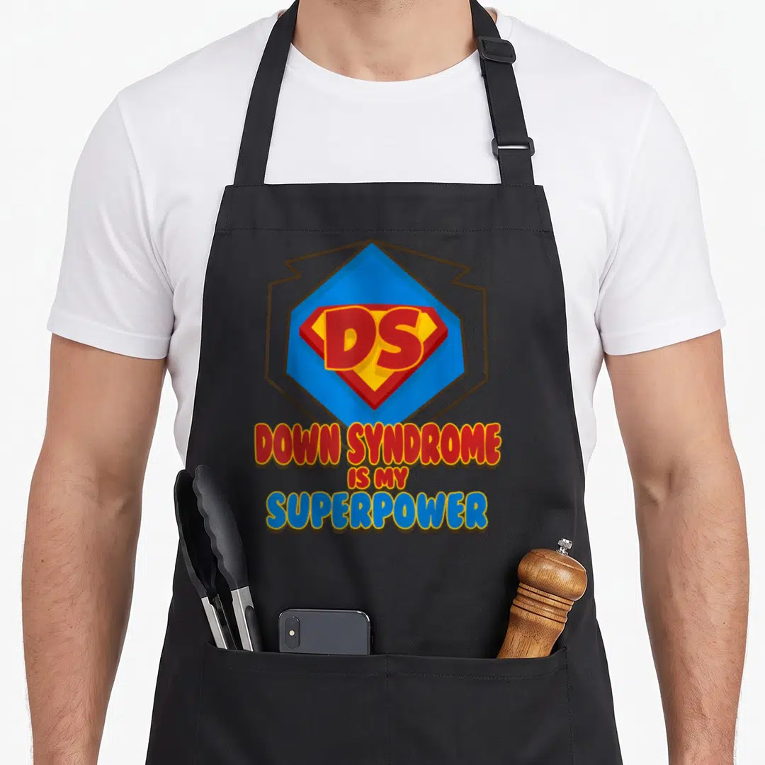 Superpower down syndrome awareness apron - Red blue yellow DS superhero shield with Down Syndrome Is My Superpower text — shown on a black cotton canvas apron against a white background