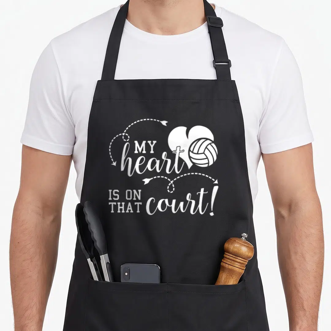 Volleyball school dad apron - White typography reading MY heart IS ON THAT court with a heart and volleyball graphic — shown on a black cotton canvas apron against a white background