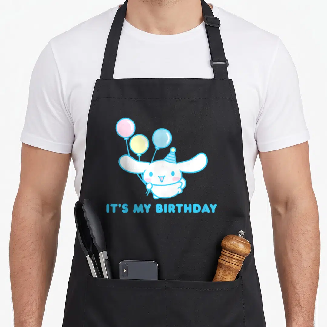 Birthday cinnamoroll apron - White creature holding three balloons with IT'S MY BIRTHDAY text in blue — shown on a black cotton canvas apron against a white background