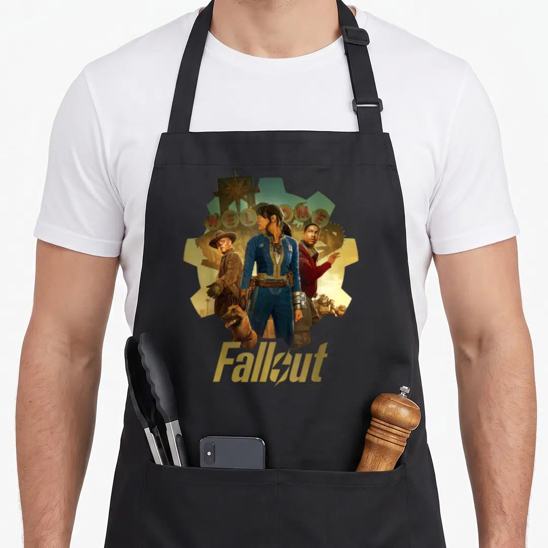 Trio vegas apron - Woman flanked by two men and a dog under WELCOME sign with Fallout logo — shown on a black cotton canvas apron against a white background