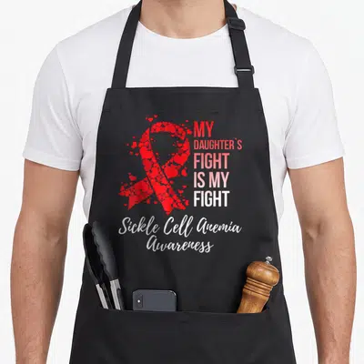 Daughter sickle cell awareness apron - Red ribbon made of hearts with My Daughters Fight Is My Fight text and Sickle — shown on a black cotton canvas apron against a white background